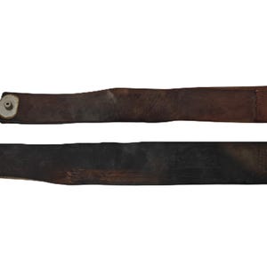 May include: Two antique leather razor strops. The top strop is brown with a curved handle and metal hardware. The bottom strop is black with a metal clasp. Both are designed for sharpening straight razors.