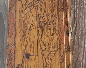 May include: A wooden box with a carved image of a person wearing a hat and coat. The image is in a rectangular frame on the front of the box.