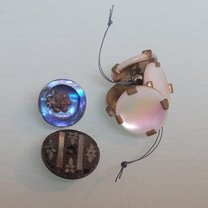 May include: Assortment of vintage buttons, including a blue iridescent button with a flower design, a brown button with silver accents, and four white iridescent buttons with gold accents.
