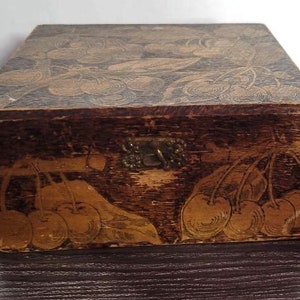 May include: A wooden box with a hinged lid and a brass latch. The box is decorated with a carved design of cherries and leaves. The box is dark brown with gold accents.