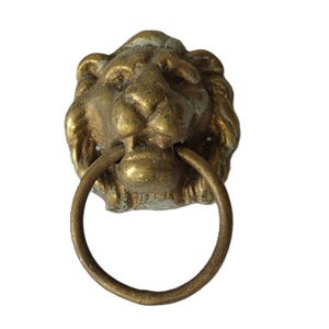 May include: Antique brass lion head door knocker with a circular handle. The lion's face is detailed with a textured mane and facial features. The knocker is mounted on a white background.