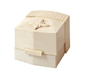 May include: A white plastic ring box with a star design on the lid. The box has a hinged lid and a small latch on the front.