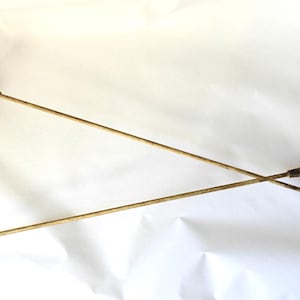 May include: Two antique fencing foils with wooden handles, red guards, and slender metal blades. The foils are crossed against a white background, showcasing their vintage design and craftsmanship. The handles are approximately 6 inches long.