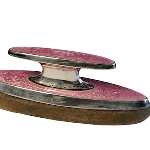 Puede incluir: Un cojín de sello ovalado de color rosa y plateado con una plataforma elevada. El cojín de sello está hecho de cuero y tiene un borde plateado. La plataforma también es plateada y tiene una parte superior de esmalte rosa. El cojín de sello está marcado con "TIFFANY & CO."