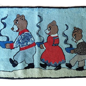 May include: A rectangular rug with a light blue background featuring three brown bears walking in a line. Each bear holds a blue bowl with rising steam. The first bear wears a blue and red outfit, the second a red dress, and the third a brown sweater.