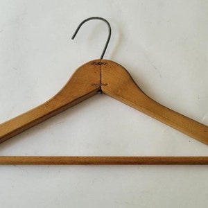 May include: A wooden clothes hanger with a metal hook. The hanger is made of two pieces of wood that are joined together at the top. The hanger is a light brown color.
