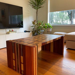 May include: A coffee table crafted from a variety of woods, featuring a distinctive patchwork design on the top. The table is rectangular in shape and stands on four legs.