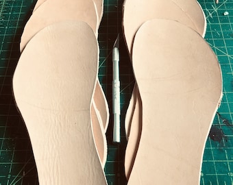 May include: Six beige leather soles for shoes or sandals, stacked on top of each other. The soles are cut out in a rounded shape.