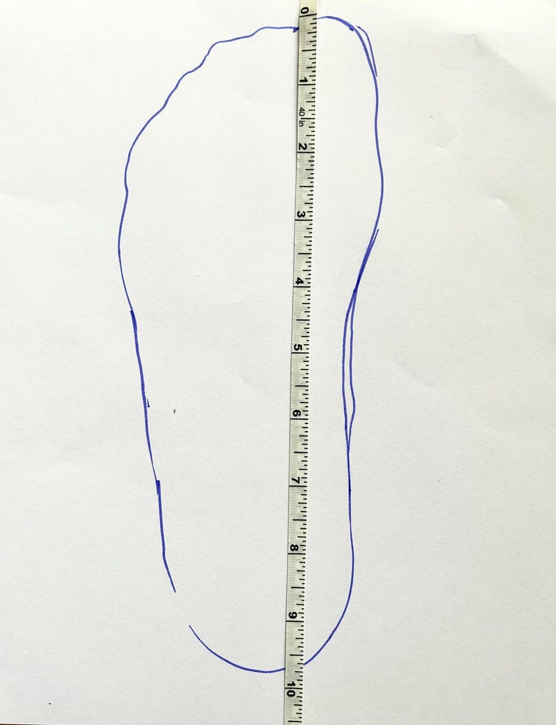 May include: A blue outline of a foot traced on white paper, with a ruler placed alongside. The ruler shows a measurement of approximately 9 inches. The image is for shoe size measurement.