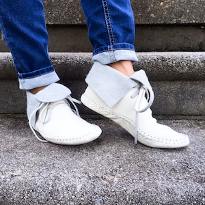 May include: White leather ankle boots with a gray suede collar and laces. The boots have a hand-stitched sole and are worn with blue jeans. The boots are a neutral color and can be worn with many outfits.