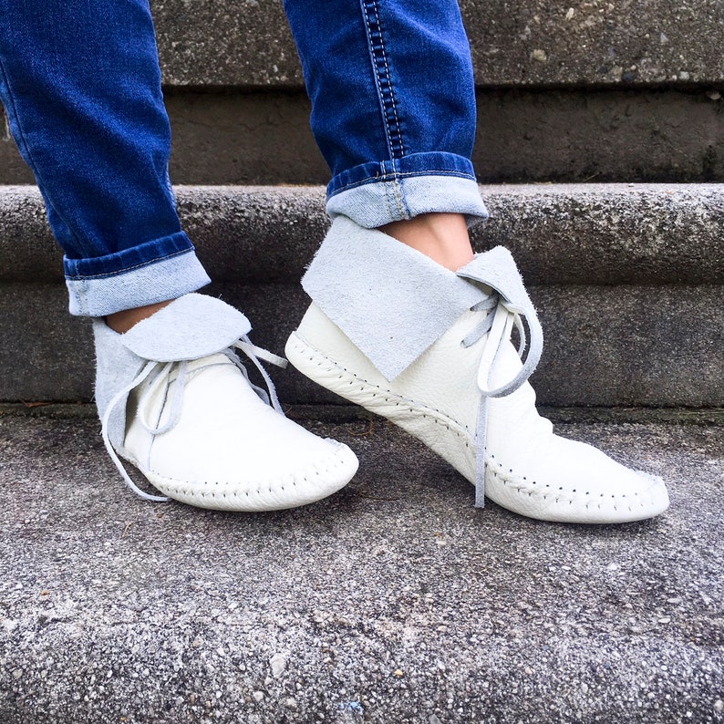 May include: White leather ankle boots with a gray suede collar and laces. The boots have a hand-stitched sole and are worn with blue jeans. The boots are a neutral color and can be worn with many outfits.