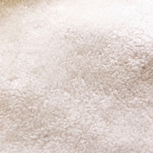 May include: Close-up of a white, fluffy, soft, and textured fabric. The fabric has a fuzzy, plush appearance.