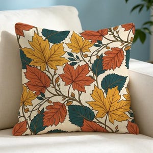 May include: A square scatter cushion featuring a repeating pattern of autumn leaves in shades of yellow, orange, and dark teal against a cream-coloured background. The design includes detailed illustrations of maple and oak leaves on thin branches.