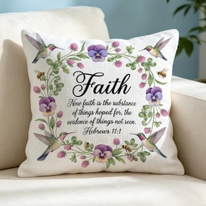 Könnte beinhalten: Ein quadratisches weißes Zierkissen mit einem zentralen Blumenkranz aus violetten Stiefmütterchen, grünem Klee und Kolibris. Der Text lautet: Faith, Now faith is the substance of things hoped for, the evidence of things not seen. Hebrews 11:1.