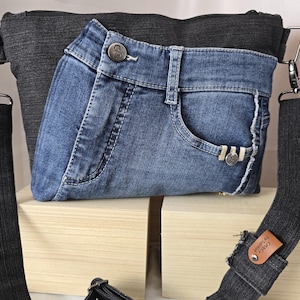 Könnte beinhalten: Eine Jeans-Umhängetasche mit einem Design einer blauen Jeans-Tasche. Die Tasche hat einen dunkelgrauen Körper und einen Riemen, mit einem silberfarbenen Knopf und Reißverschluss. Der Riemen hat ein kleines braunes Lederetikett mit der Aufschrift "Cuky by Sabihah".