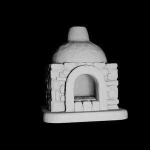 Può includere: Una scultura in miniatura di un forno con finitura bianca opaca, caratterizzata da un esterno a blocchi testurizzati simili alla pietra, un'apertura centrale ad arco e una cupola arrotondata, poggiante su una base rettangolare piatta.