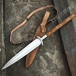 Könnte beinhalten: Ein langer Dolch mit silberner Klinge, Holzgriff und Lederscheide. Der Griff ist geschnitzt und die Scheide ist braun. Ein Lederriemen ist befestigt. Die Länge beträgt ca. 40 cm.