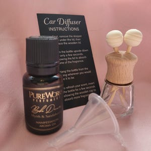 May include: A brown glass bottle of PureWorks Perfumery Myrrh & Sandalwood aroma oil, a clear glass car diffuser bottle with a wooden lid and two small wooden sticks, a small plastic funnel, and a black instruction card titled Car Diffuser.