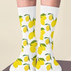 Könnte beinhalten: Weiße Socken mit einem sich wiederholenden Muster aus gelben Zitronen mit grünen Blättern. Die Socken werden mit einer gelben Hose getragen. Die Zitronen sind leuchtend gelb und gleichmäßig verteilt.