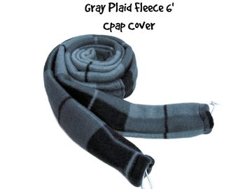 May include: A gray plaid fleece CPAP cover measuring 6 feet in length. The fabric features a dark gray and black checkered pattern. The tubular cover is coiled and includes thin white drawstrings at the ends for securing the CPAP hose.