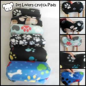 May include: A set of six colourful fleece crutch pads with paw print designs. The pads are stacked on top of each other and feature different colours and patterns, including black, blue, green, red, and white. The pads are designed to provide comfort and support for crutches.