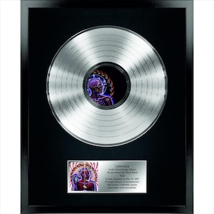 Peut inclure: Disque de platine encadré de l'album "Lateralus" du groupe Tool. Le disque est argenté avec une image centrale d'une figure humaine avec un cerveau et des organes internes. Le cadre est noir, et une plaque en dessous détaille les informations sur l'album.