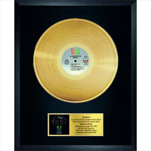 May include: Framed gold record of Queensrÿche's "Empire" album. The record is displayed in a black frame with a gold plaque below, which includes album details and the band's logo. The record label is visible.