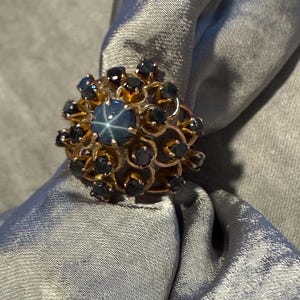 May include: A gold ring with a large blue star sapphire surrounded by smaller black sapphires.