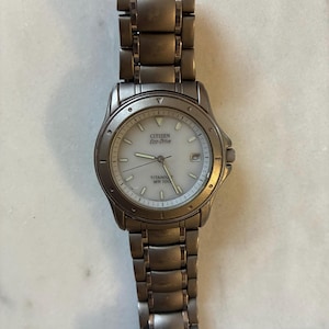 May include: A titanium Citizen Eco-Drive watch with a white face and silver hands. The watch has a date display and a silver band. The watch face has the text "CITIZEN Eco-Drive TITANIUM WR 100".