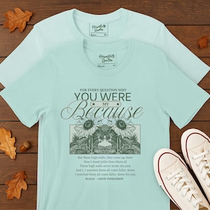Op de afbeelding: Twee lichtblauwe t-shirts met de tekst "FOR EVERY QUESTION WHY YOU WERE MY Because" en een zonnebloemontwerp. De shirts bevatten ook een citaat uit Louis Tomlinsons nummer "Walls".