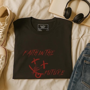 May include: Dark grey t-shirt featuring the red text "FAITH IN THE FUTURE" and a graphic design. The shirt is displayed on a bed, accompanied by white trainers, headphones, and a notebook.
