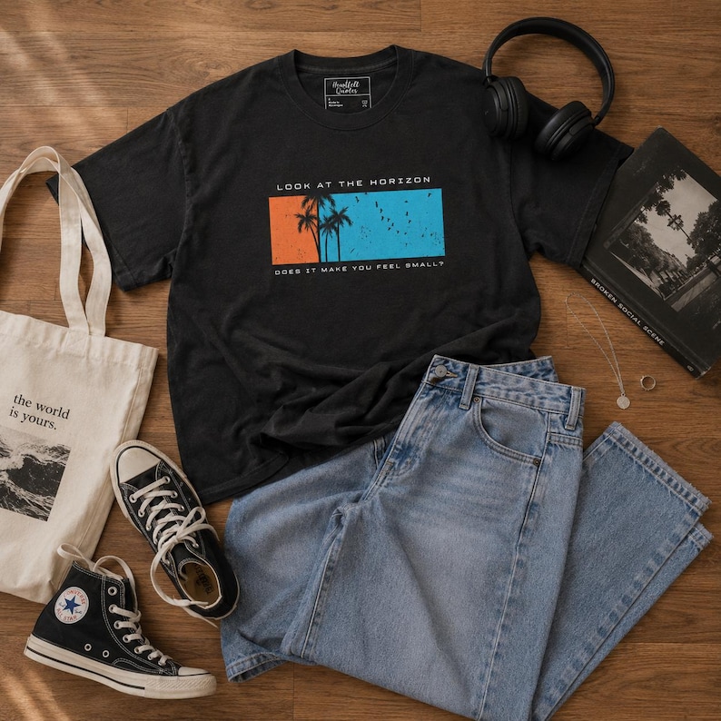 K&ouml;nnte beinhalten: Ein schwarzes T-Shirt mit einem Grafikdruck, der Palmen vor einem orange-blauen rechteckigen Hintergrund zeigt, mit dem Text LOOK AT THE HORIZON und DOES IT MAKE YOU FEEL SMALL? Eine hellblaue Jeans, eine Stofftasche und Turnschuhe.