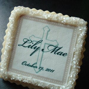 May include: A white sugar cookie with a green cross and the text "Lily Mae October 19, 2011".