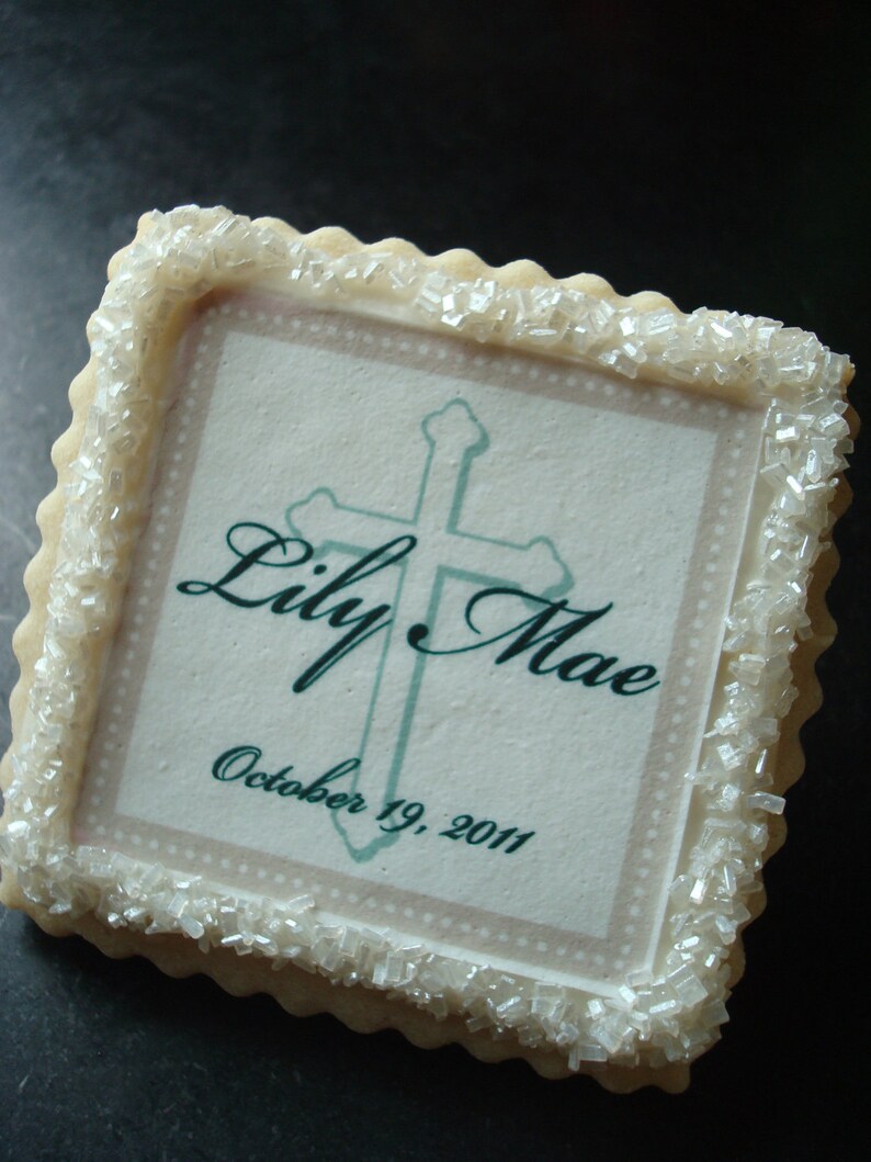 May include: A white sugar cookie with a green cross and the text "Lily Mae October 19, 2011".