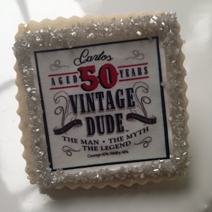 K&ouml;nnte beinhalten: Ein dekorierter Zuckerkeks mit silbernen Streuseln an den R&auml;ndern. Der Keks hat ein bedrucktes Design mit dem Text "Carlos Aged 50 Years Vintage Dude Experience The Man The Myth The Legend Courage 60% Ability 40%"