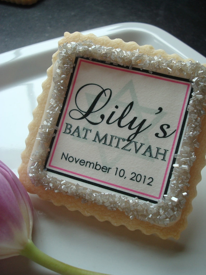 Pu&ograve; includere: Un biscotto bianco con spolverata di zucchero argentato e un bordo nero attorno a un cartoncino bianco con il testo "Lily's Bat Mitzvah November 10, 2012".