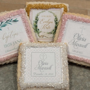 May include: Four decorated sugar cookies with pink and white frosting. The cookies feature different designs and text, including "baptism", "Iris Jane", "God Bless Evelyn Kate", "Olivia Maxwell", and a cross.