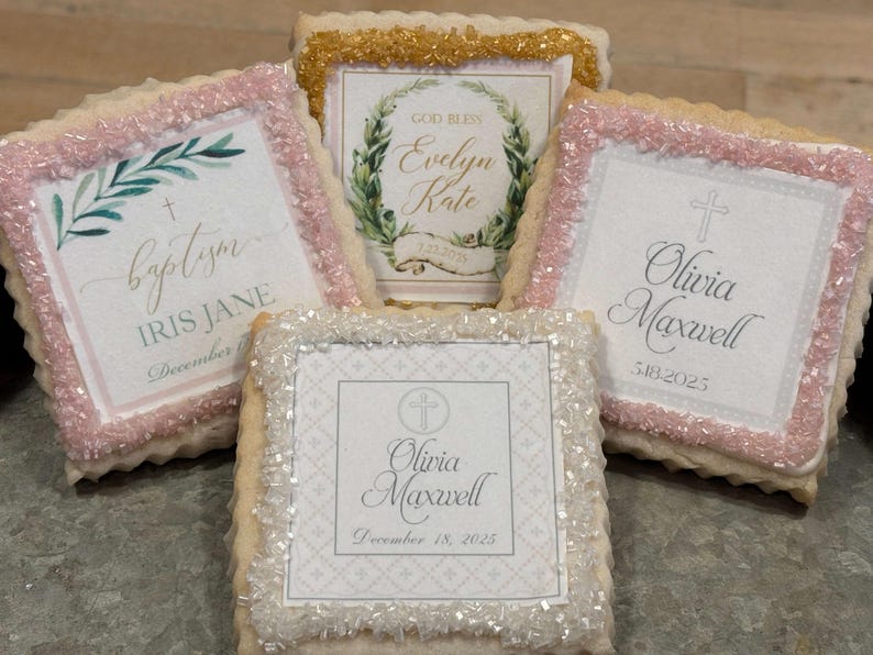 May include: Four decorated sugar cookies with pink and white frosting. The cookies feature different designs and text, including "baptism", "Iris Jane", "God Bless Evelyn Kate", "Olivia Maxwell", and a cross.