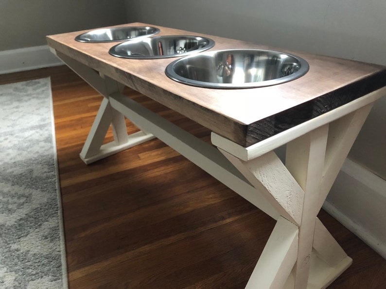 May include: A wooden dog bowl stand with three stainless steel bowls. The stand has a white painted base with a rustic wood top.