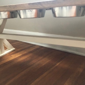 May include: White wooden table with a distressed wood top. Three stainless steel dog bowls are attached to the underside of the table.
