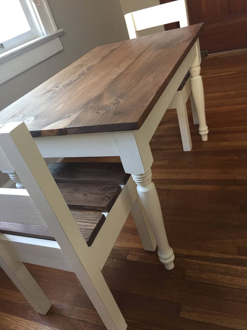May include: A small wooden table with a dark brown tabletop and white legs. The table has a classic design, with turned legs and a simple, functional style. The table is approximately 30 inches long and 20 inches wide.