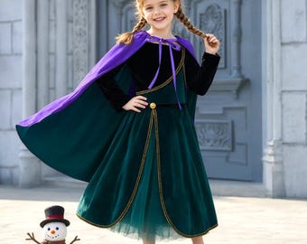 Può includere: Un abito in velluto nero a maniche lunghe con gonna verde scuro, mantello viola e corona dorata. L'abito presenta finiture dorate sul corpetto e sulla gonna, e un bottone dorato in vita. Una piccola statuetta di pupazzo di neve si trova accanto.