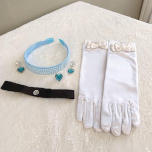 May include: A light blue headband with a white checkered pattern, two heart-shaped blue earrings, a black ribbon choker with a central clear stone, and a pair of white satin gloves featuring small white bows at the wrists.