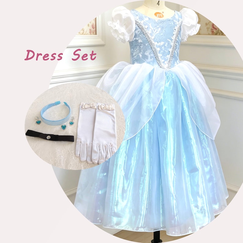 May include: A light blue dress set featuring a floor-length gown with white puff sleeves, a silver sequin bodice, and a sheer white overskirt. Accessories include a light blue headband, heart-shaped earrings, a black choker, and white gloves.