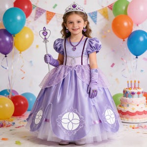 May include: A young girl in a lavender princess costume, complete with a tiara, jewelry, and gloves, smiles in front of a colorful balloon backdrop. The dress features decorative accents and a flowing skirt, perfect for a birthday party or dress-up play.