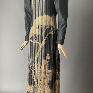 May include: A long black and gold dress with a tree and floral print. The dress has long sleeves with puffed shoulders and a fitted bodice.