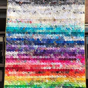 May include: A colorful quilt with a rainbow pattern made of many different fabric scraps. The quilt is made in a wavy pattern and has a yellow border.