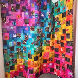 May include: A colorful quilt with a rainbow gradient pattern. The quilt is made up of many small squares, each with a different design. The quilt is hanging on a wall.