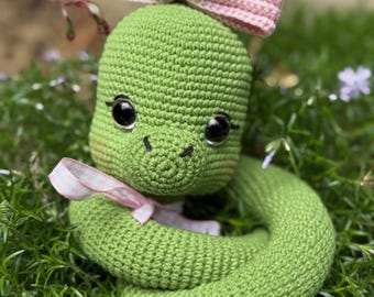 Encantadora serpiente verde de ganchillo con lazo rosa y diseño flexible, juguete amigurumi hecho a mano