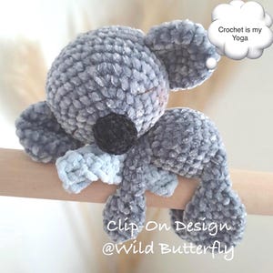 Könnte beinhalten: Ein graues Koala-Plüschtier aus weichem Samtgarn mit schwarzer Nase und geschlossenen Augen. Der Koala ist an einem Holzstab befestigt. Eine weiße Sprechblase enthält den Text "Crochet is my Yoga". Der Text darunter lautet "Clip-On Design @Wild Butterfly".